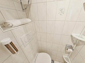 A small, modern bathroom with white tiles, a toilet, a shower area, and a towel rack.