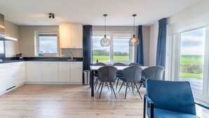 Uma cozinha moderna com armários brancos, bancada preta e um espaço de refeições com cadeiras cinzas e um sofá azul.