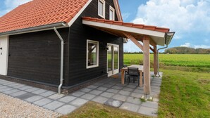 Uma casa moderna com telhado de telhas vermelhas, um alpendre coberto com mesa e cadeiras, e vista para um campo verde.