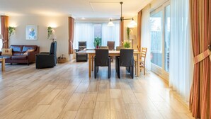 A modern living room with a dining area, wooden flooring, and large windows with curtains. - Inviting Villa in Panningen (Panningen)