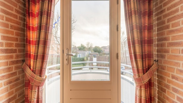 A door with a view of a residential area, flanked by brick walls and plaid curtains. - Inviting Villa in Panningen (Panningen)
