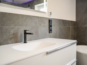 A modern bathroom with a white sink, black faucet, and grey tiles. - High-quality Apartment With Whirlpool (Bramberg am Wildkogel)