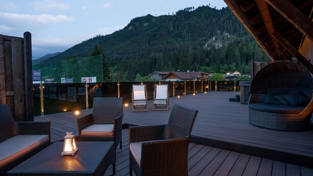 A wooden deck with wicker furniture and a hanging chair, overlooking a mountainous landscape. - High-quality Apartment With Whirlpool (Bramberg am Wildkogel)