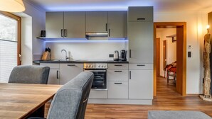 A modern kitchen with grey cabinets, a built-in oven, and a coffee maker. There is a dining table with chairs and a wooden floor. - High-quality Apartment With Whirlpool (Bramberg am Wildkogel)