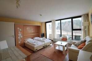 A hotel room with a bed, a sofa, a small table, and a window with a view of trees.