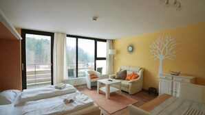 A hotel room with two beds, a sofa, a small table, and a view of the outdoors. - Apartment in Freyung Near Bavarian Forest (Freyung)