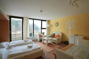A hotel room with two beds, a sofa, a small table, and a view of the outdoors. - Apartment in Freyung Near Bavarian Forest (Freyung)