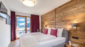 A bedroom with a large bed, wooden panel walls, a view of mountains, and a balcony. - Luxurious Flat in a Great Location on the Hochkonig (Muehlbach Am Hochkoenig)