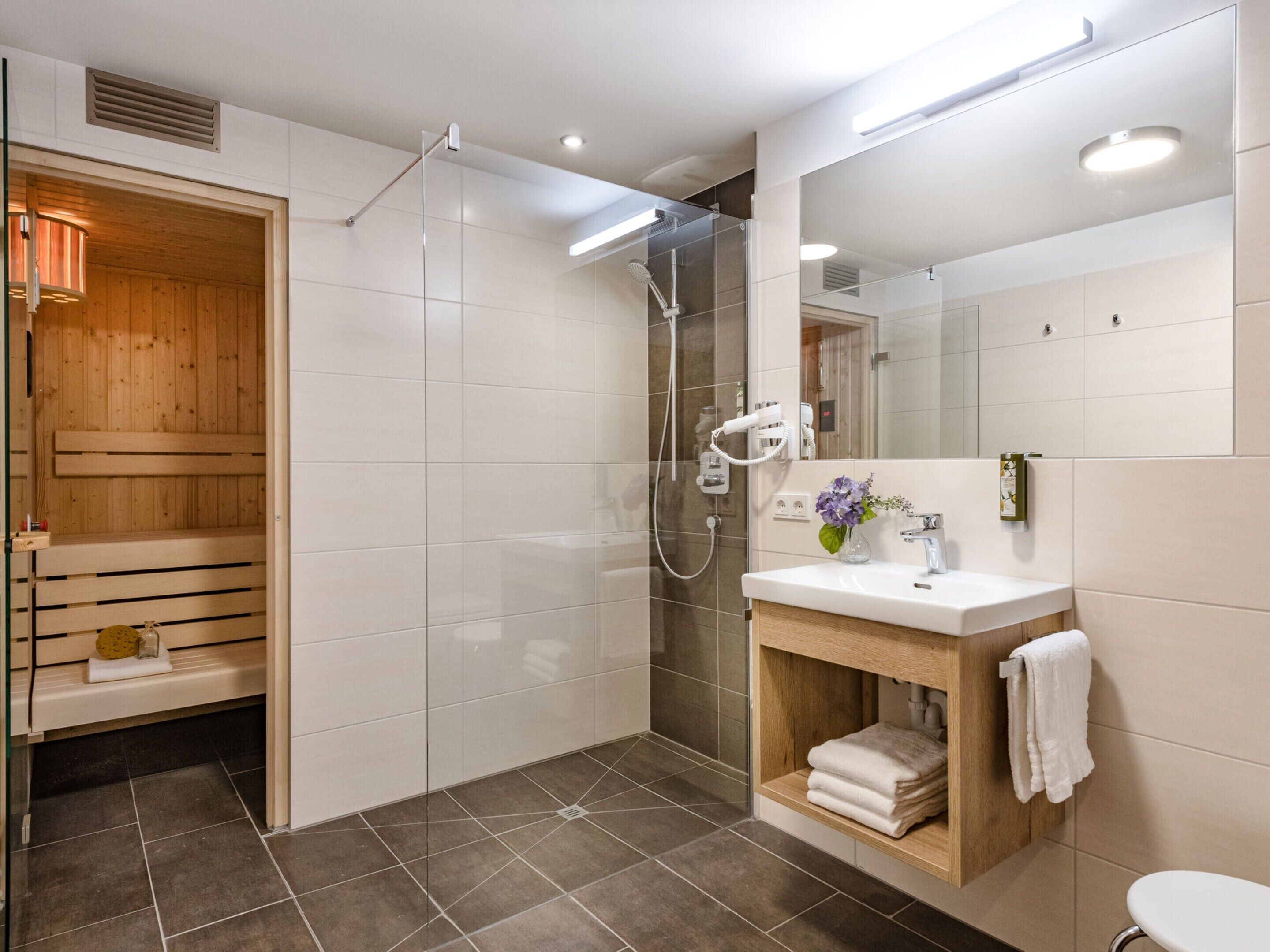 Une salle de bain moderne avec une douche à parois de verre, un sauna en bois et un lavabo blanc avec un miroir.