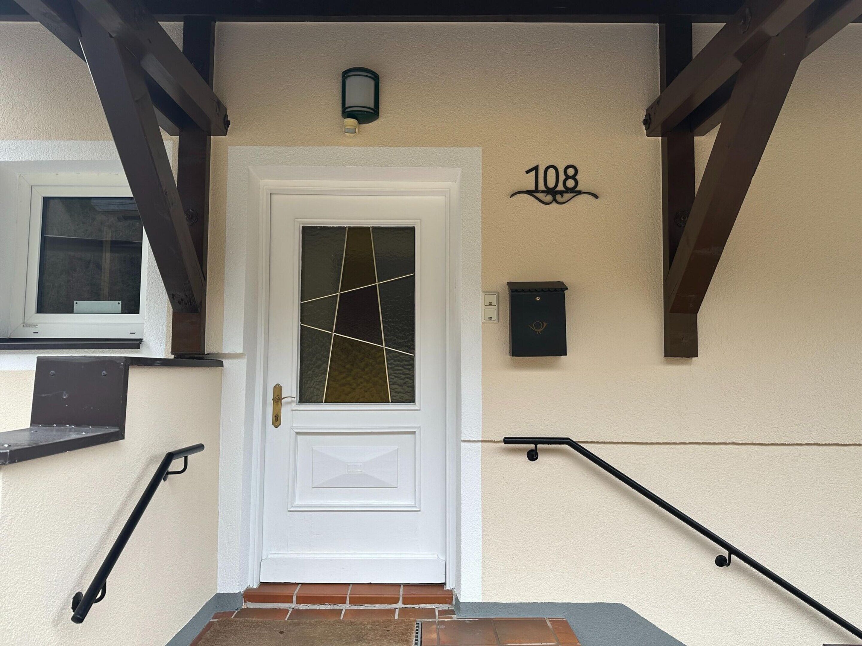 A white door with a glass panel, a number '108' above it, a small mailbox, and a window to the left.