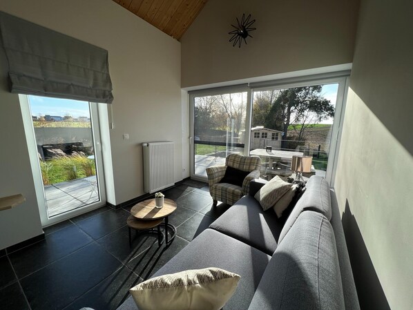 A modern living room with a large sliding glass door, a sectional sofa, a small round table, and a radiator.