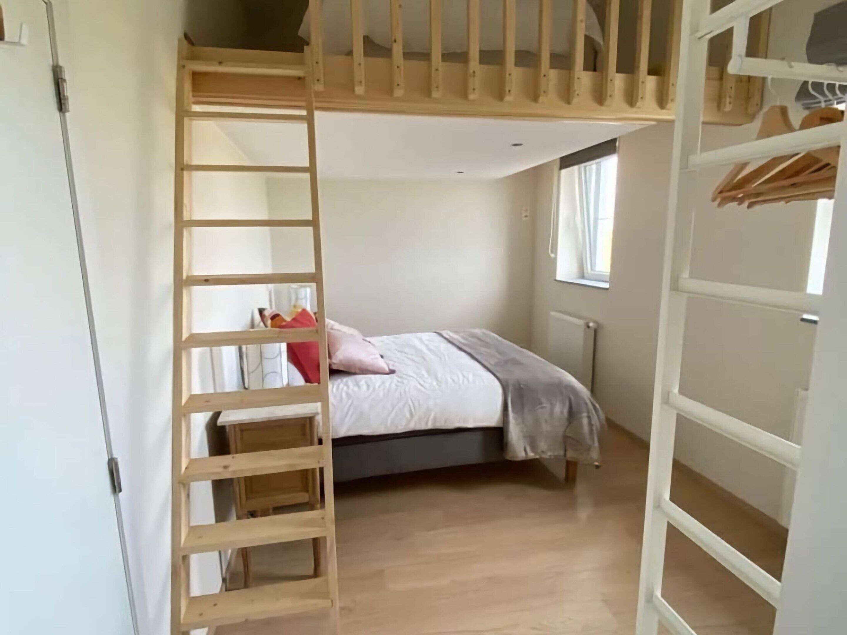 A bedroom with a bunk bed, a wooden ladder, a window, and a radiator.