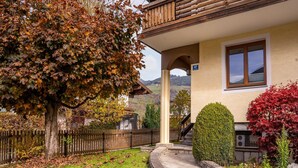 Una casa con un camino de piedra que lleva a la entrada, rodeada por una valla de madera y un árbol con hojas otoñales.