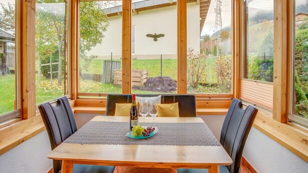 Un comedor con mesa y sillas de madera, vista al exterior y una escultura de pájaro en la pared.