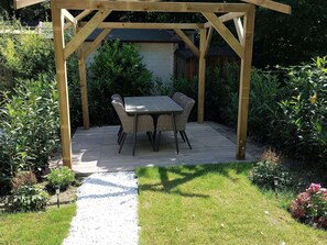 A wooden pergola with a table and chairs in a garden setting.