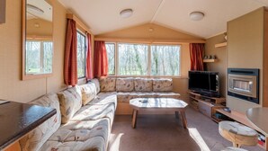 Interior aconchegante de uma motorhome, com sofá seccional, mesa pequena, televisão e área de cozinha compacta.