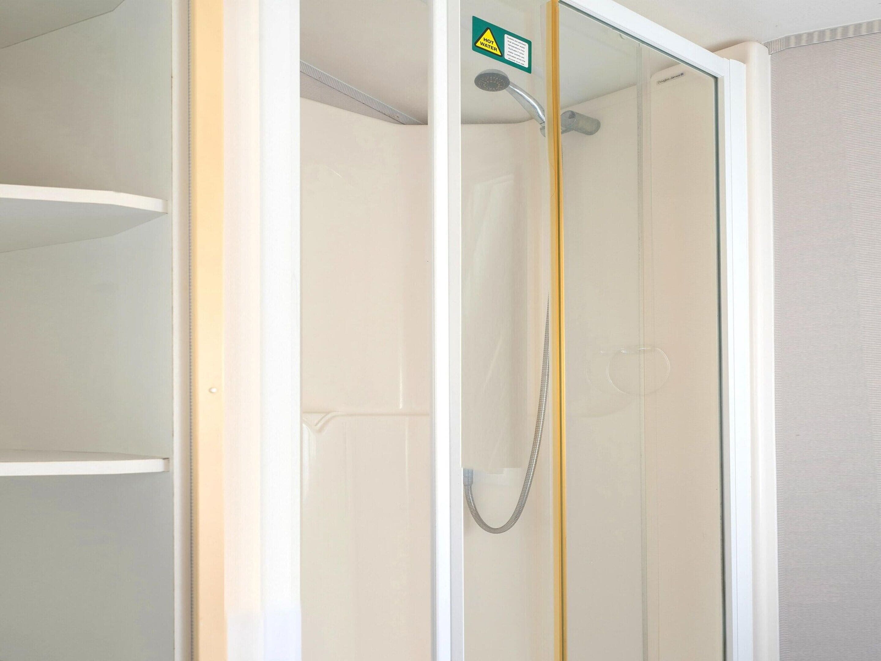 Un box de ducha con paredes de vidrio, un letrero de advertencia de agua caliente, un cabezal de ducha y una manguera.