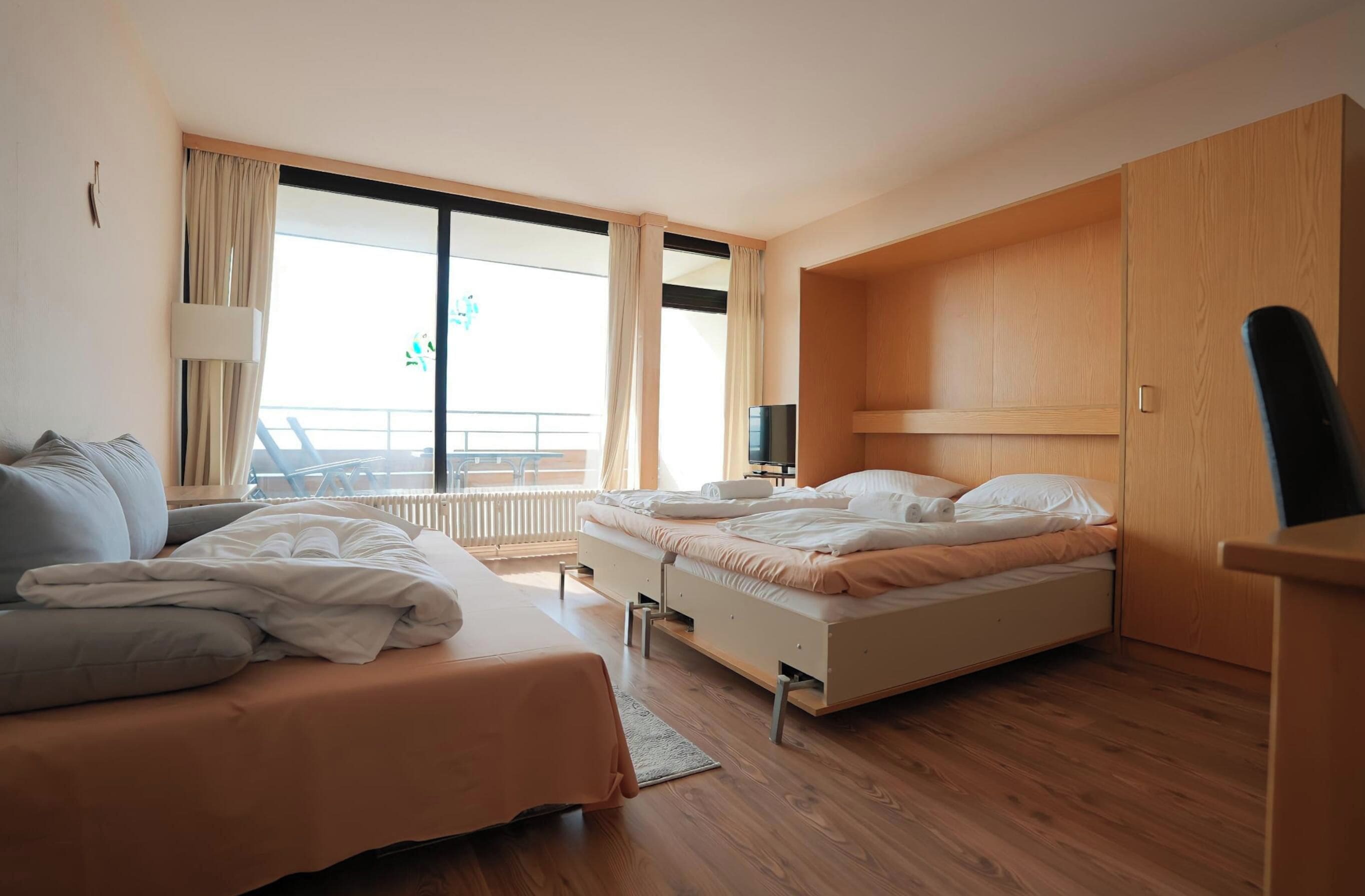 Une chambre d’hôtel avec deux lits, une grande fenêtre, un balcon et une armoire en bois.