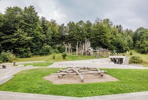 A park with a modern building, a grassy area with a sculpture, and a forest in the background.