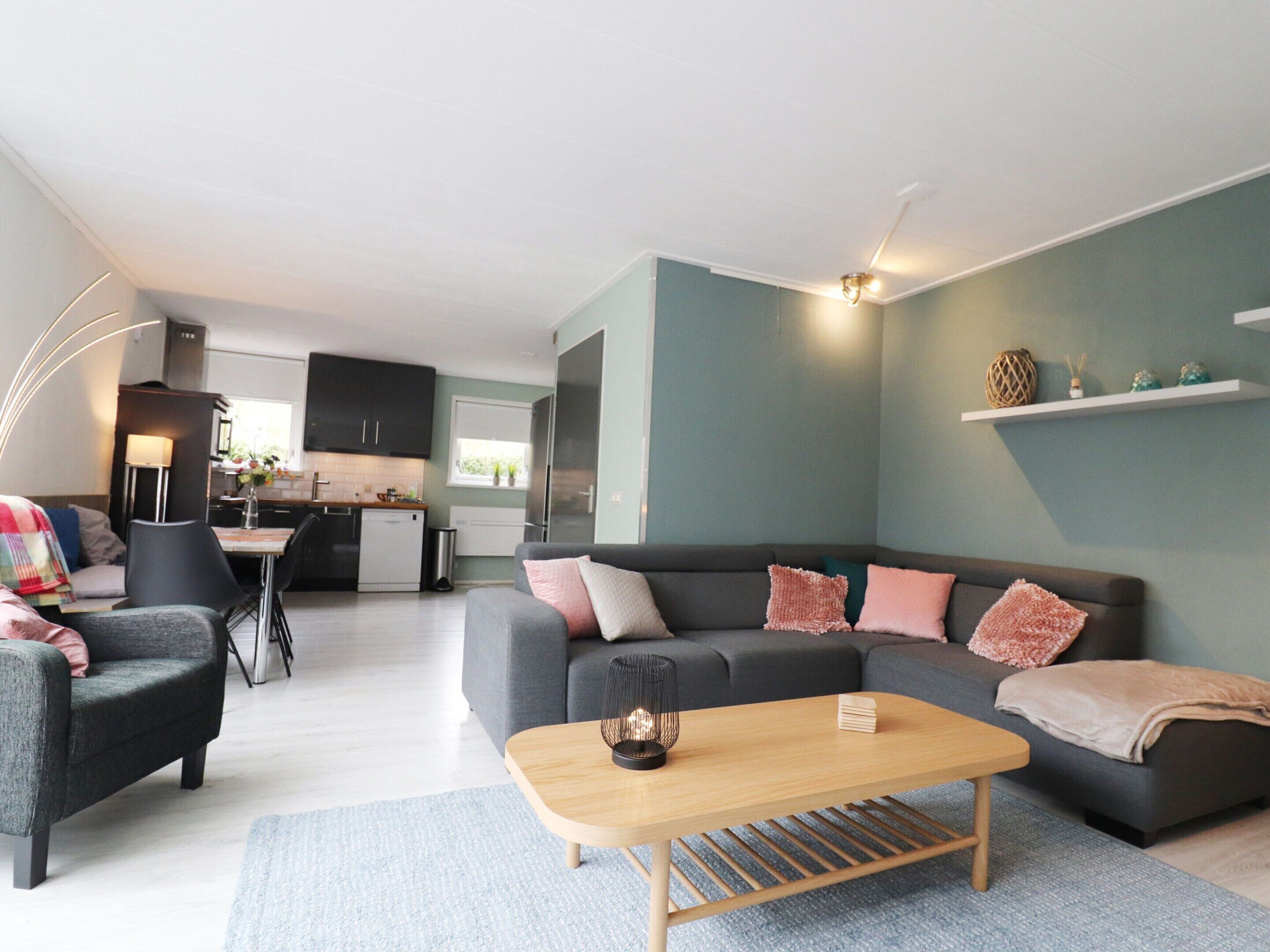 A modern living room with a grey sofa, a wooden coffee table, and a kitchen in the background.