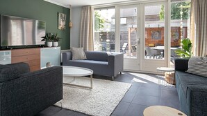 A modern living room with a flat-screen TV, grey sofas, a white coffee table, and a large sliding glass door leading to an outdoor patio. - Holiday Home in Grou With Bubble Bath (Grou)