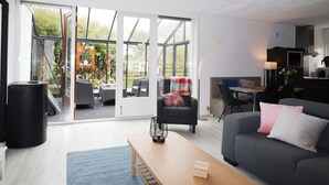 A modern living room with a sofa, a coffee table, and a dining area with chairs. There is a sliding glass door leading to a garden. - Holiday Home in Grou With Bubble Bath (Grou)