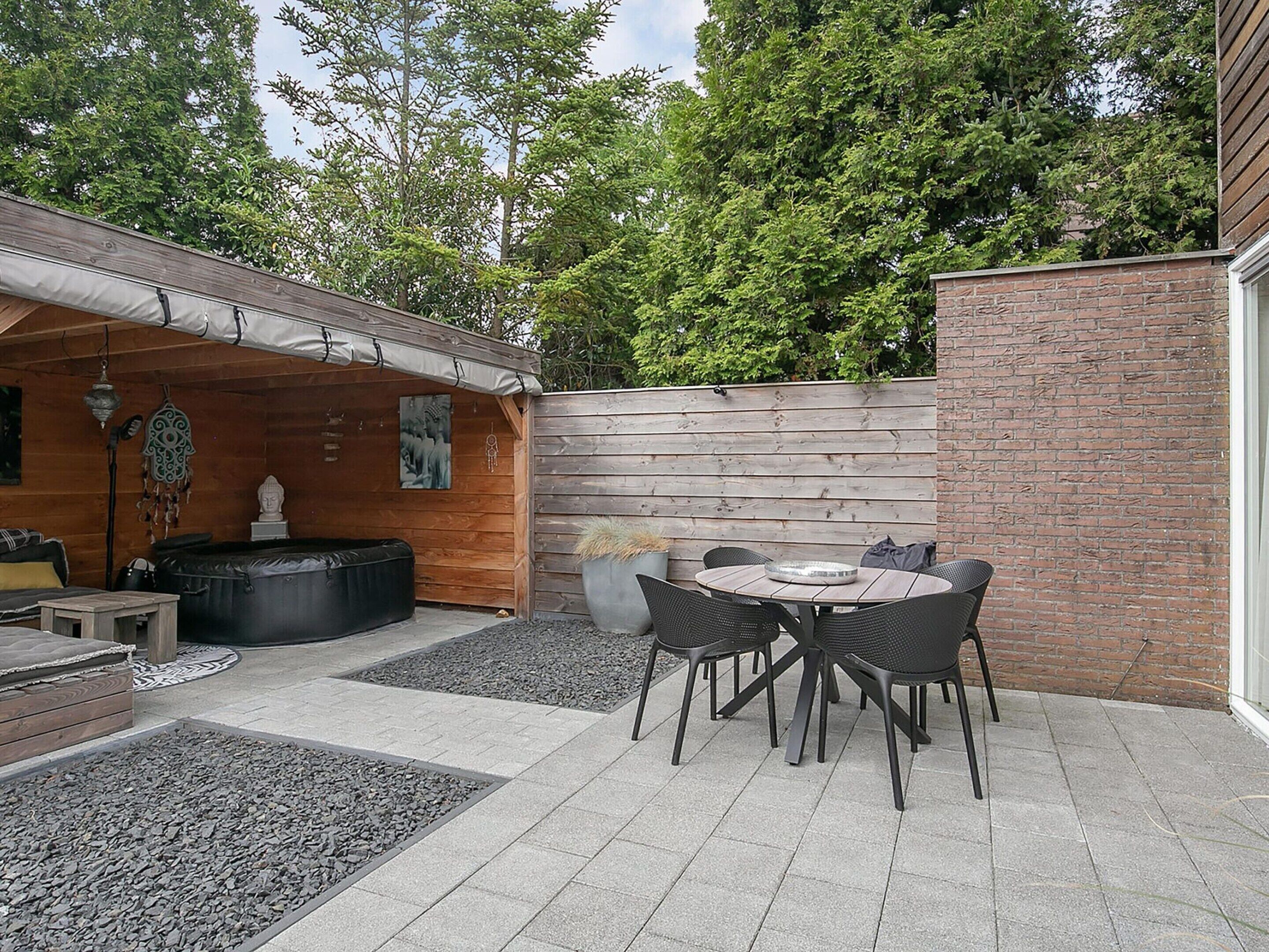 A patio area with a round table and chairs, a wooden deck, and a brick wall.