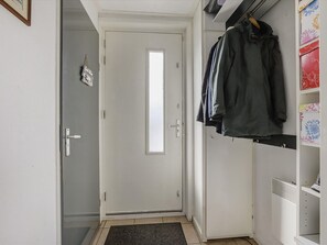 A hallway with a white door, a coat rack with several jackets, and a white shelving unit with patterned boxes.