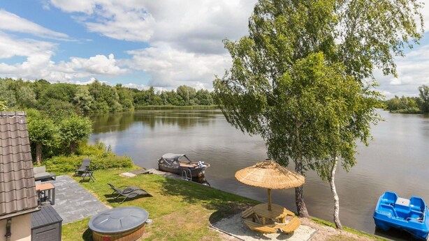 A lakeside patio with a boat, lounge chairs, and a barbecue grill.