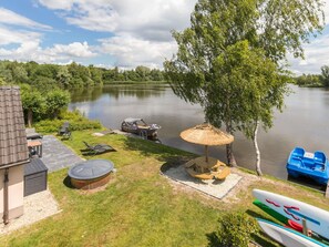 A lakeside patio with a boat, lounge chairs, and a barbecue grill. - Family House With Wellness (Vlagtwedde)
