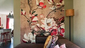 A living room with a large floral mural on the wall, a brown sofa, and a red chair.