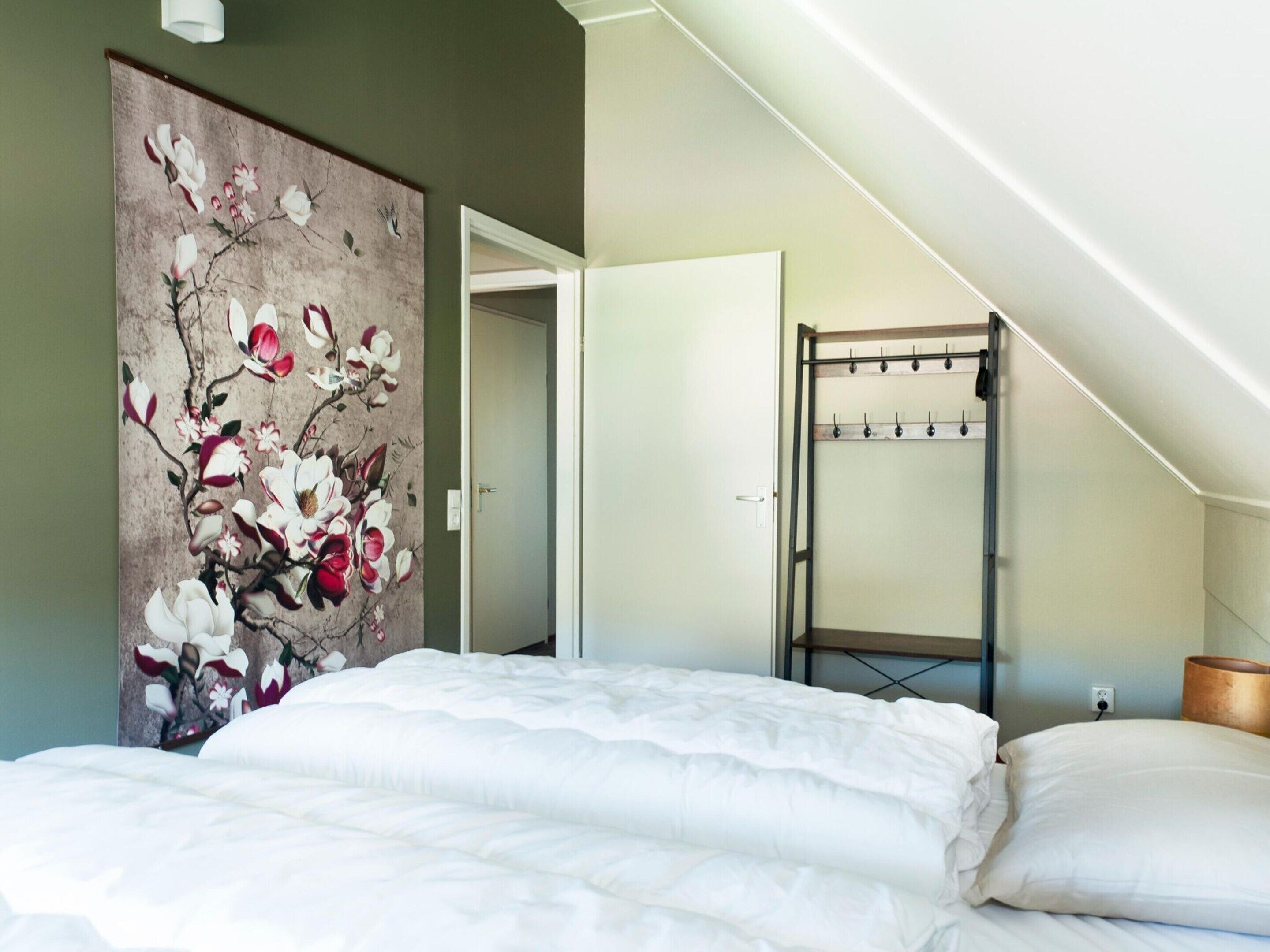 A bedroom with a bed, a coat rack, and a door leading to another room.