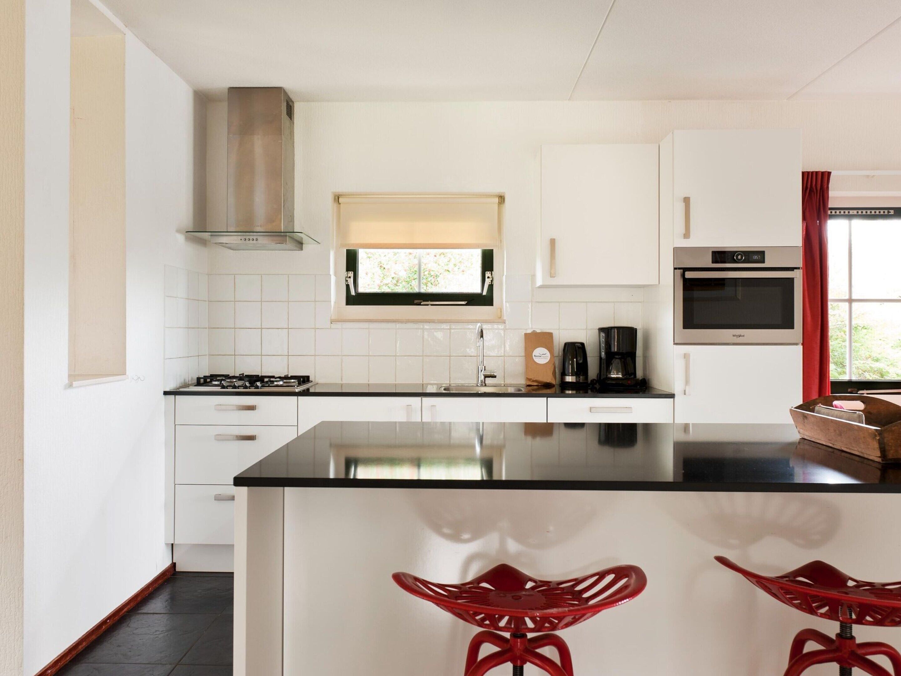 A modern kitchen with white cabinets, a black countertop, a built-in stove, a coffee maker, and a red chair.