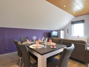 A dining area with a table set for four, a television in the background, and a window with a view. - Comfortable Apartment in Burg-reuland With Shared Terrace (Burg-Reuland)