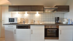 Ett modernt kök med vita skåp, vitvaror i rostfritt stål, en inbyggd ugn, en mikrovågsugn, en kaffebryggare och en vattenkokare.
