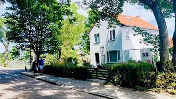 A residential street with a white house numbered 33, paved sidewalks, and lush greenery.