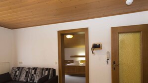 A cozy room with a sofa, a dining table with fruit, a wooden door, and a bunk bed in the background. - Apartment With Sauna in Radstadt (Radstadt)