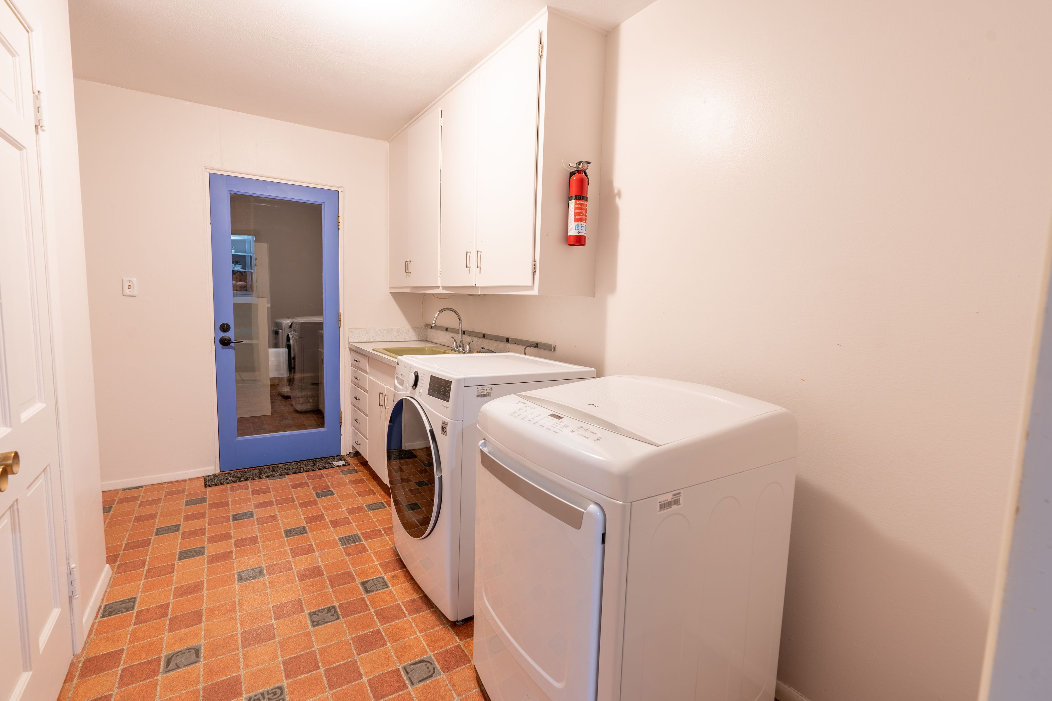 Une buanderie équipée d’un lave-linge, d’un sèche-linge et d’un extincteur fixé au mur.