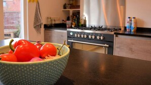 Une cuisine équipée d’une cuisinière, d’un four et d’un saladier rempli de tomates posé sur le plan de travail.