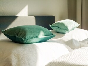 A bed with two pillows, one green and one white, in a room with a neutral color scheme.