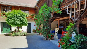 A rustic wooden building with a covered garage, potted plants, and a red car parked inside. - Loft-like Apartment With Swimming Pond (Scheibbs)