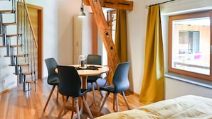 A room with a bed, a dining table with chairs, a staircase, and a window with curtains. - Loft-like Apartment With Swimming Pond (Scheibbs)