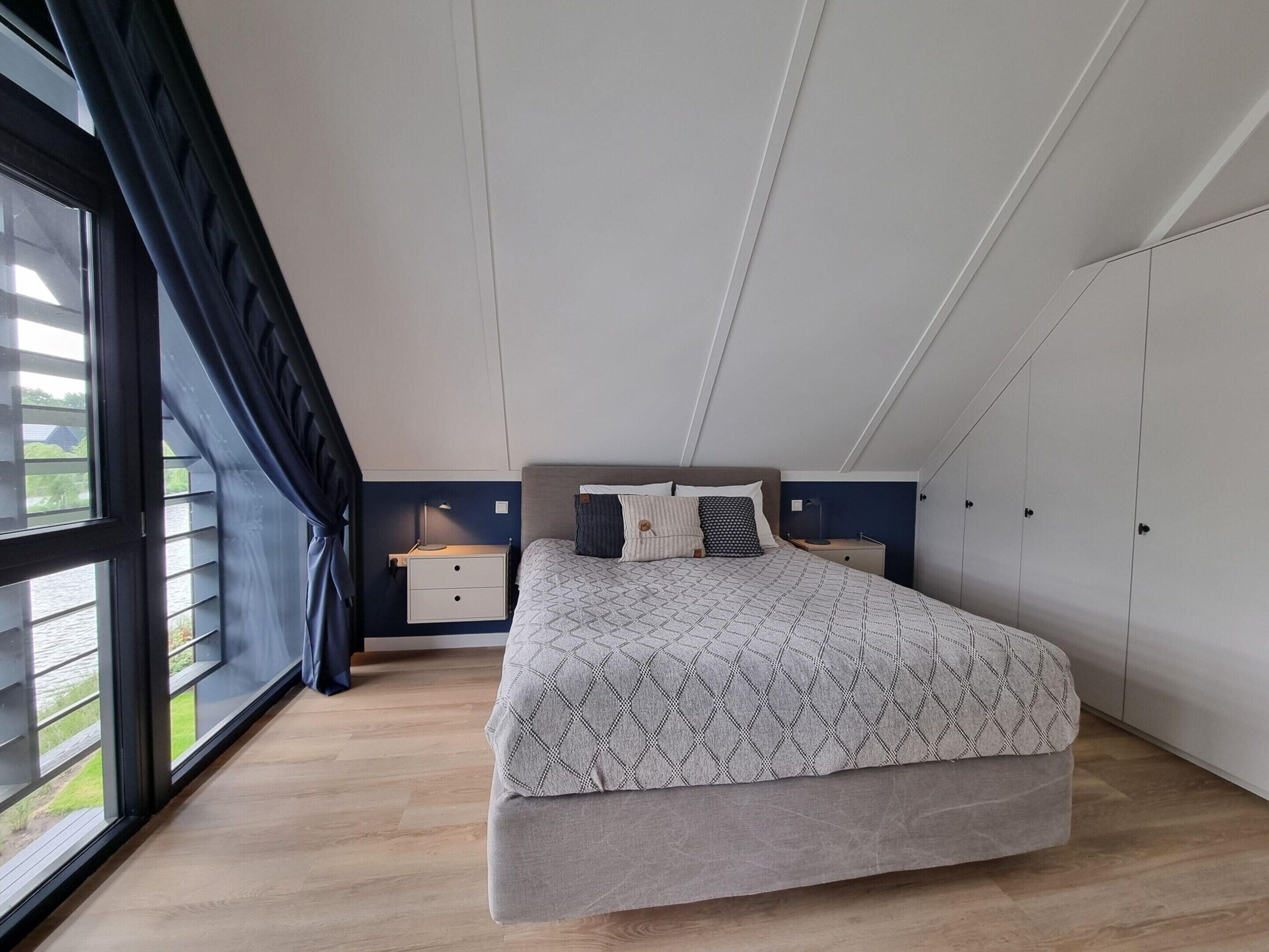 A bedroom with a bed, nightstands, a wardrobe, and a large window.