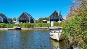 Un canal bordé de deux bâtiments modernes, avec un bateau et une végétation luxuriante tout autour.