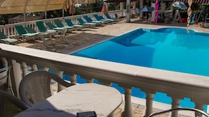 A pool area with lounge chairs and umbrellas, a covered seating area, and a stone-tiled deck. - Apartment in Mpenitses Near Beaches & Pool (Corfu)