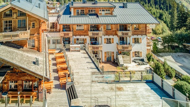 A multi-story wooden building with a restaurant sign, a wooden deck with benches, and a mountainous backdrop. - Chalet in Mittersill by Ski Lift & Sauna (Mittersill)