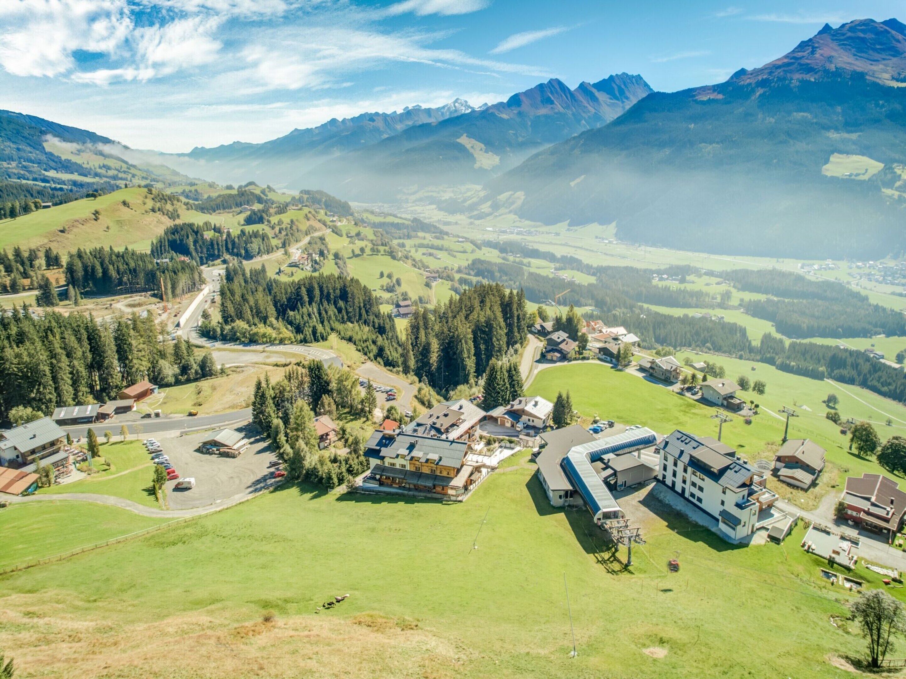An aerial view of a small town with a mix of residential and commercial buildings, surrounded by lush green hills and mountains.