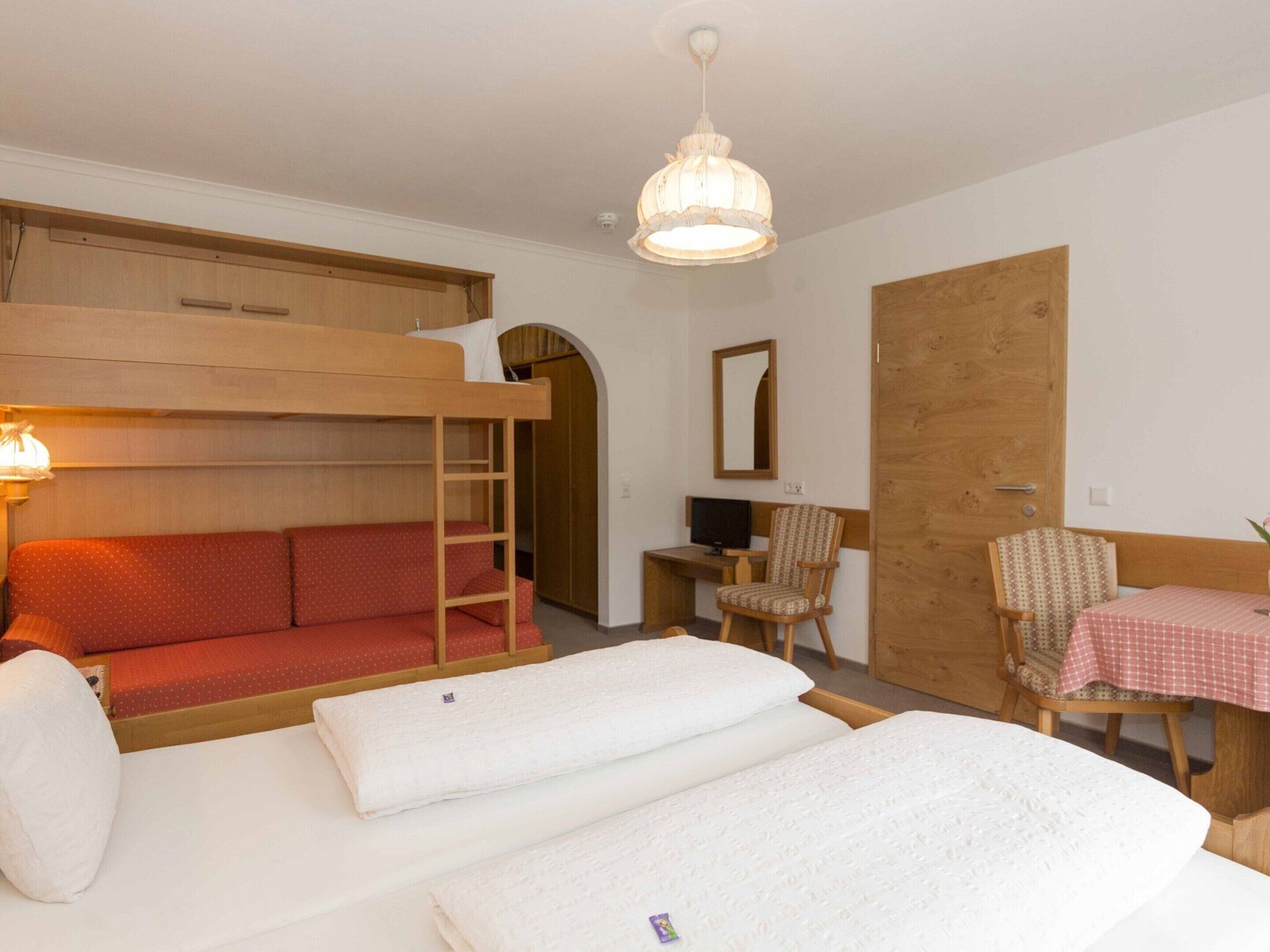 Una habitación con literas, un escritorio, una silla y una pequeña mesa con mantel a cuadros.