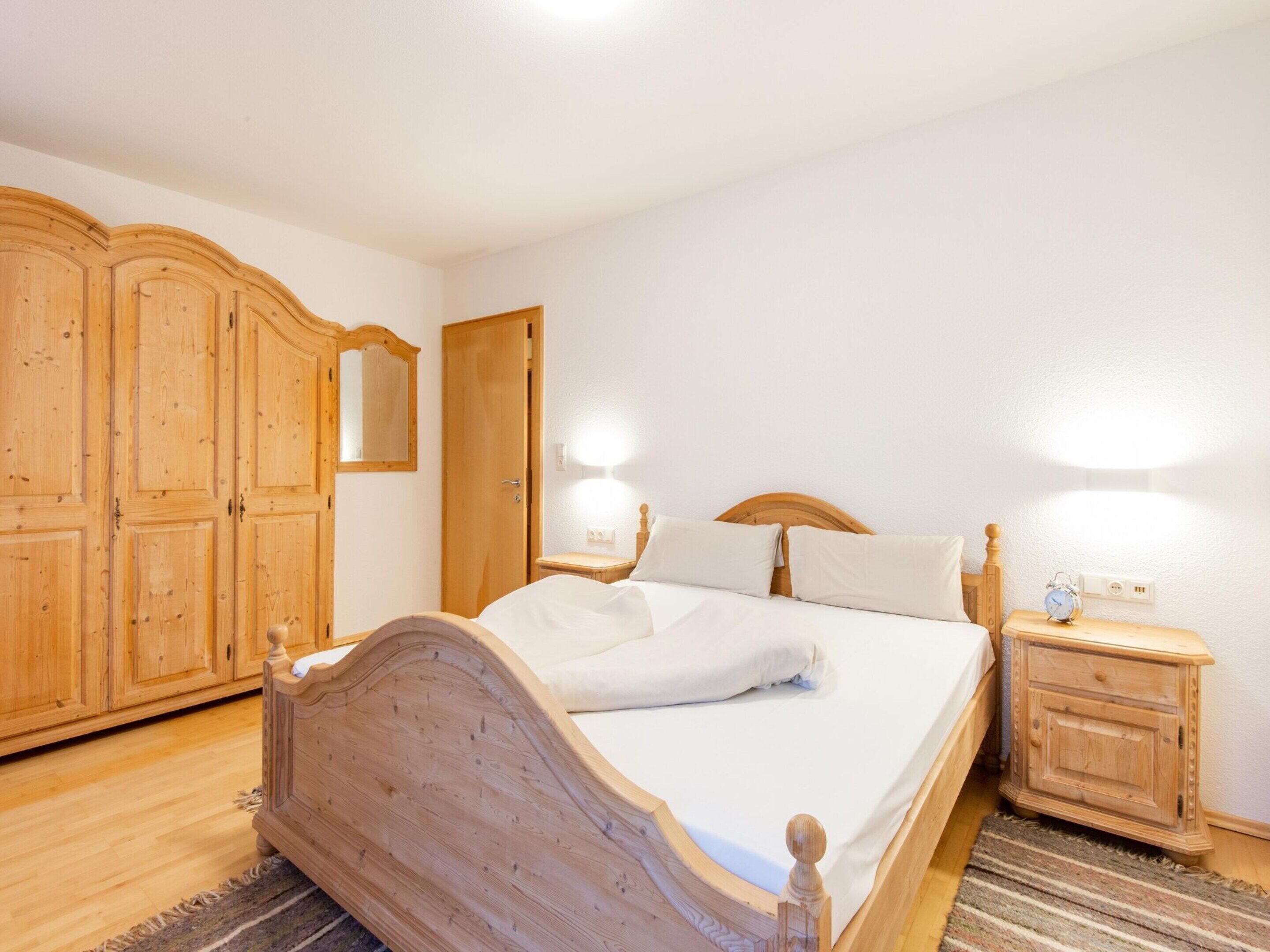 Une chambre à coucher avec un lit en bois, une table de chevet avec une horloge, une armoire et un miroir.