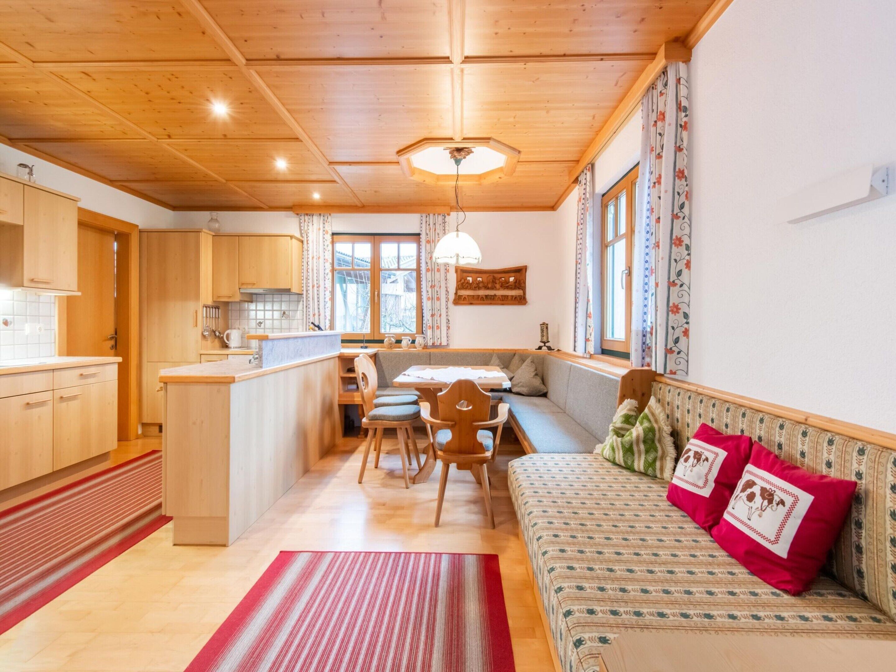 A cozy, well-lit kitchen with wooden cabinets, a dining area with a bench, and a sofa with decorative pillows.